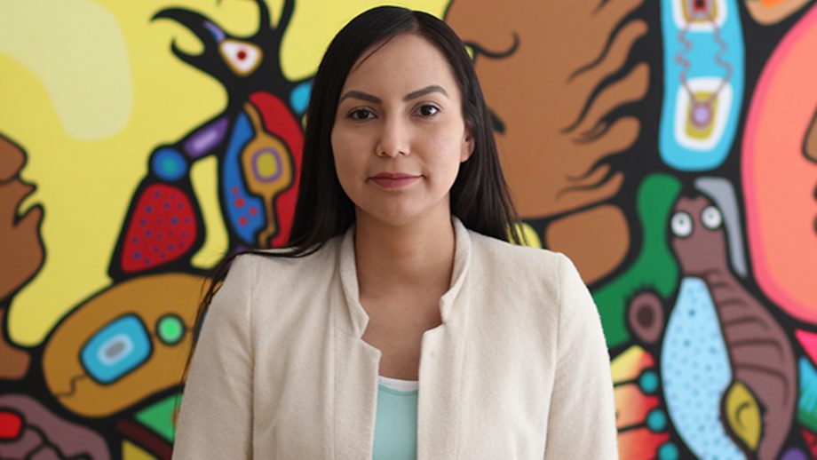 Angeline Nelson standing in front of an Indigenous painting