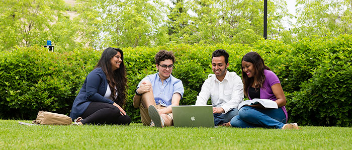 四个温尼伯大学的学生在前面的草坪上看着笔记本电脑